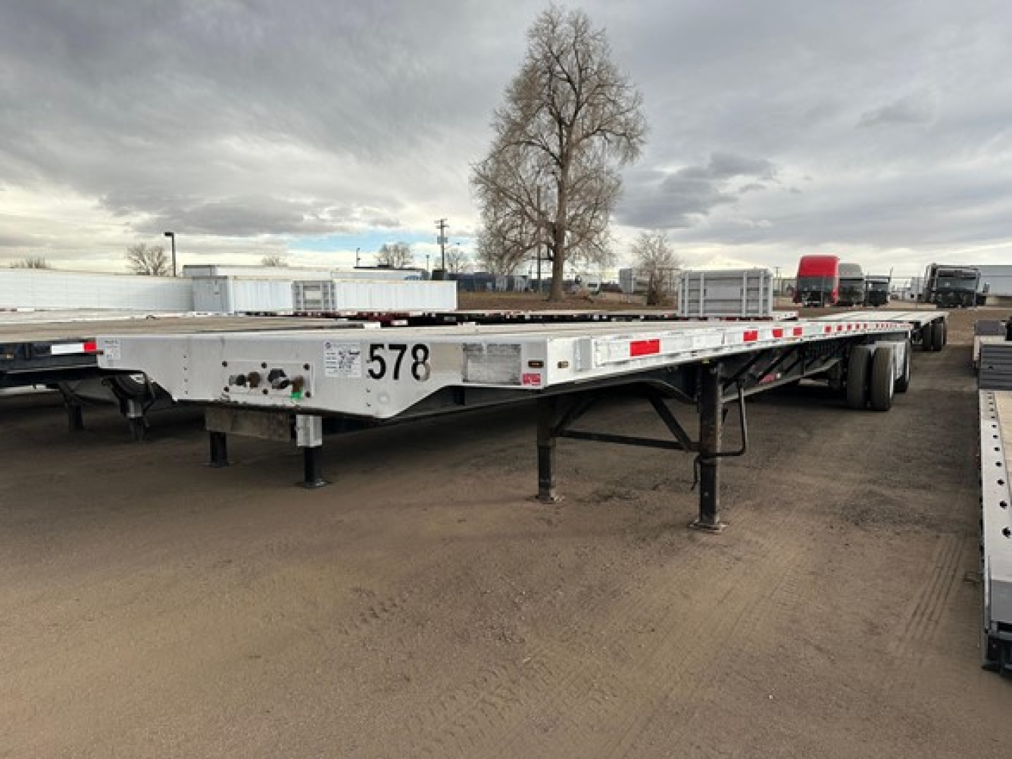 Flatbed trailer showing long low deck with landing legs down, stock number 578 and rear wheels visible.