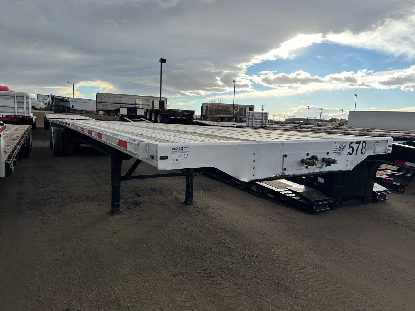 Combo flatbed trailer showing the front corner with registration markings and a lowered access ramp.