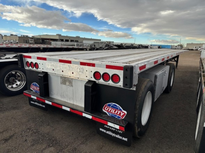 Transcraft flatbed trailer rear/side view showing dual rear axles, aluminum deck, red and white reflective tape, Utility brand mud flaps, and spare wheel area.