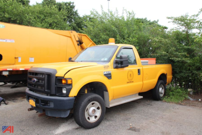 Ford F-250 Super Duty pickup truck in yellow 4x4 parked beside an orange utility vehicle, showing side view with crew cab and utility bed.