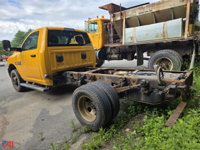 Ram 3500 cab and chassis with yellow crew cab and dump truck in background, chassis frame exposed, front axle with dual wheels, in outdoor lot.