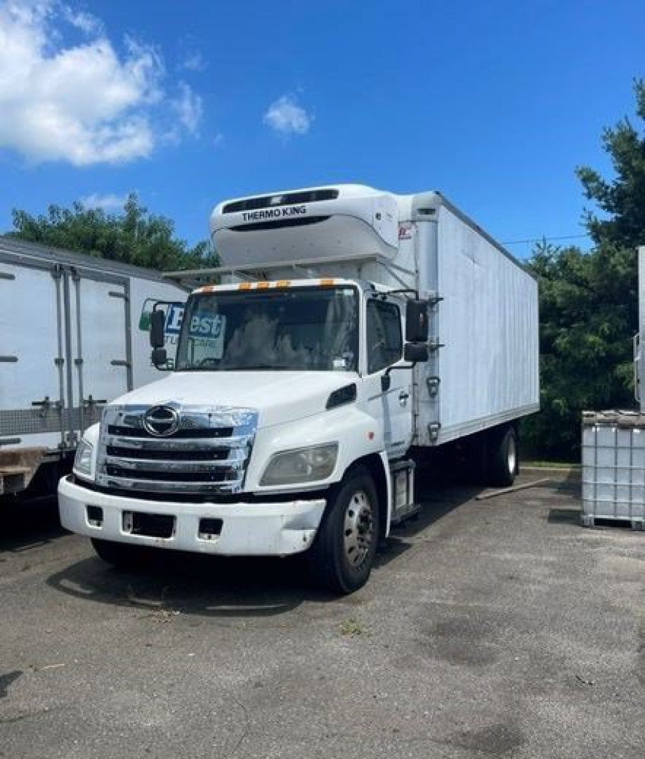 Truck front and side view of a white 2014 Hino refrigerated box truck with Thermo King unit, docked in a lot.