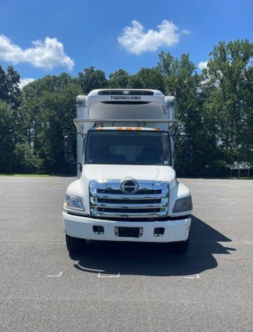Hino 258/268 reefer truck front view showing Thermo King refrigeration unit on cab roof, chrome grille, white body, clear sky.