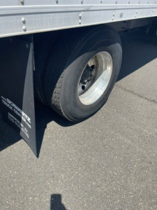 Rear wheel and side panel of a used 2014 Hino 258/268 reefer truck showing dual rear wheels and aluminum cargo body with mudflap.