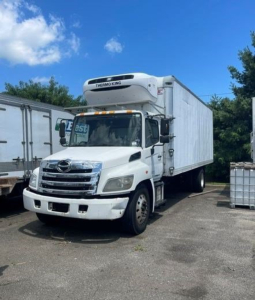 Truck with Thermo King reefer unit on top, hood with chrome grille, white cab, large box trailer in a parking lot.