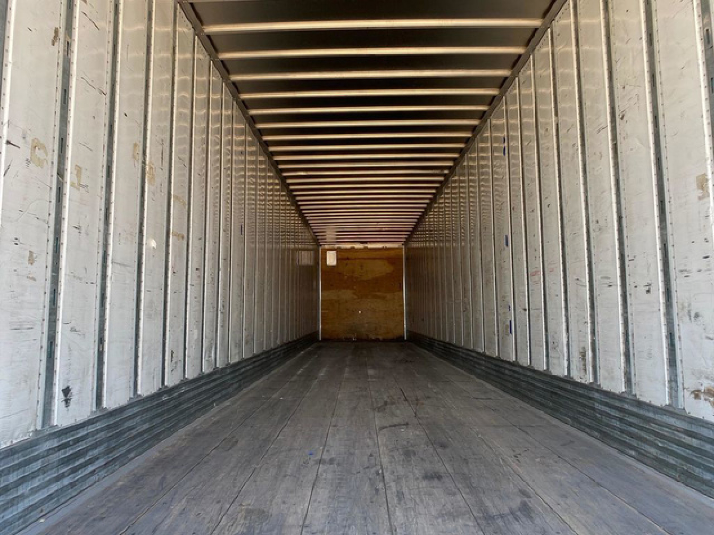 Interior view of a blank cargo trailer trailer space with metal side walls and wooden rear door, showing empty interior