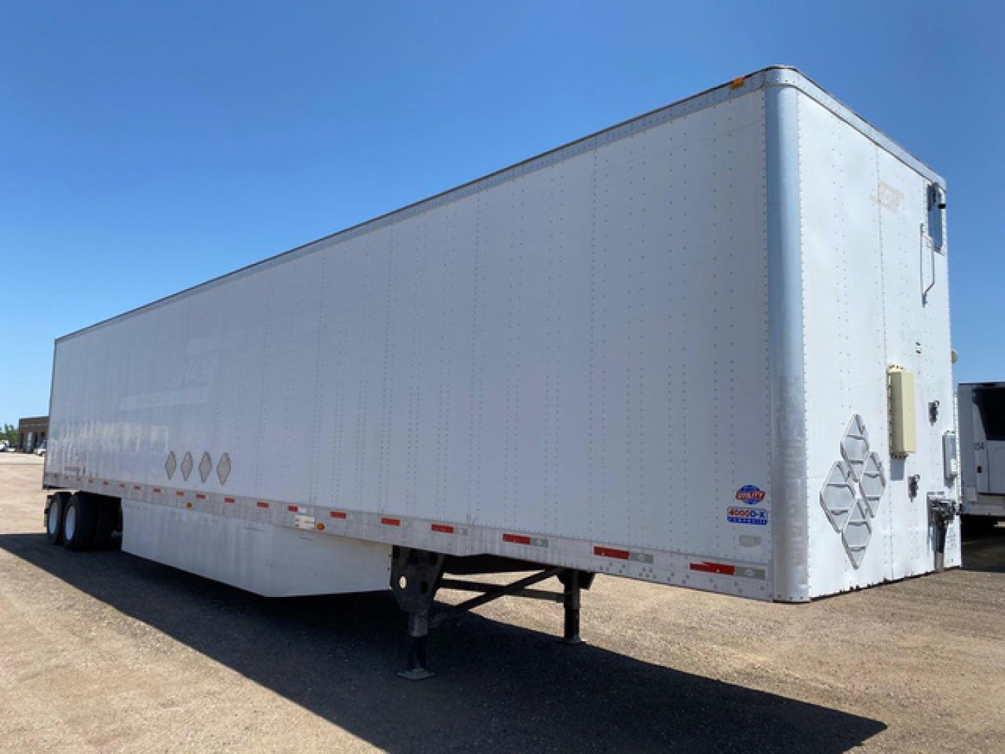 Utility van trailer showing side profile with landing gear, rear doors, and various decals. Visible text includes no legible brand names or numbers from this view.
