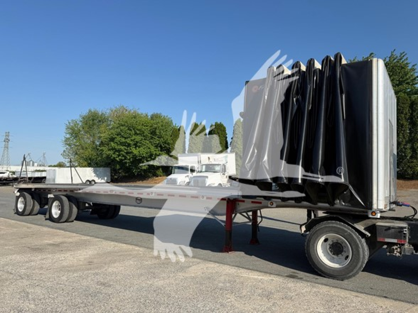 2013 Mac Alum Flat trailer with curtainside folded, long flatbed, dual rear axles, truck yard setting.