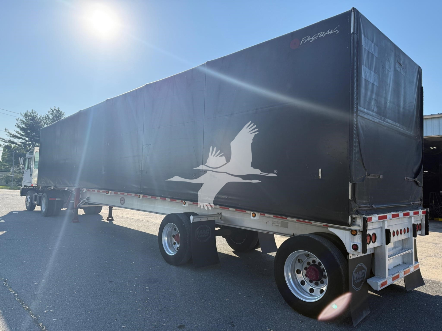 Trailer side view showing curtainside trailer with black fabric and white bird graphic, rear dual tires, rear lights, and reflective trim.