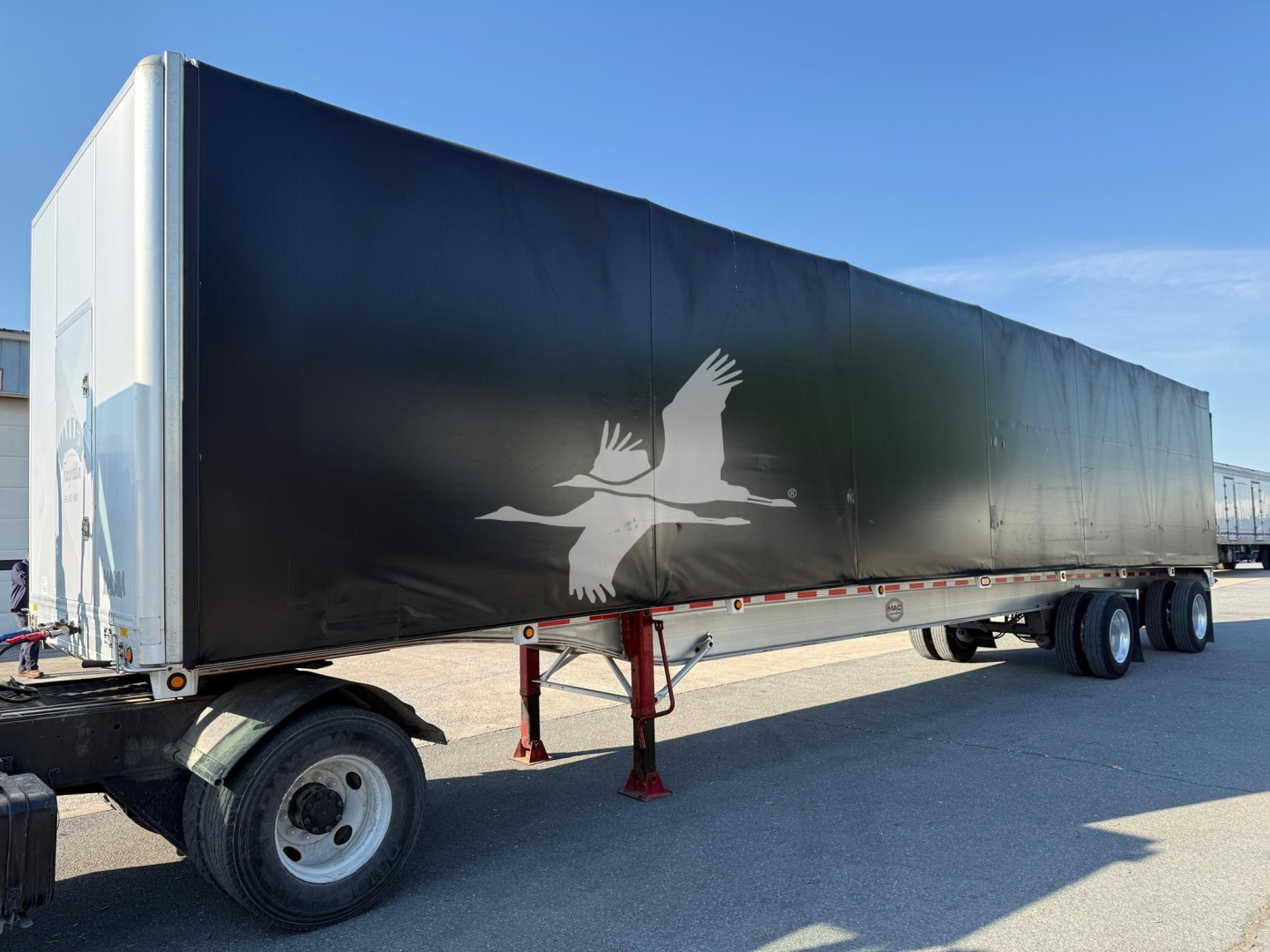 Curtainside trailer in service, side view showing black graphic with white birds and logo, 3-axle wheels visible, light blue sky