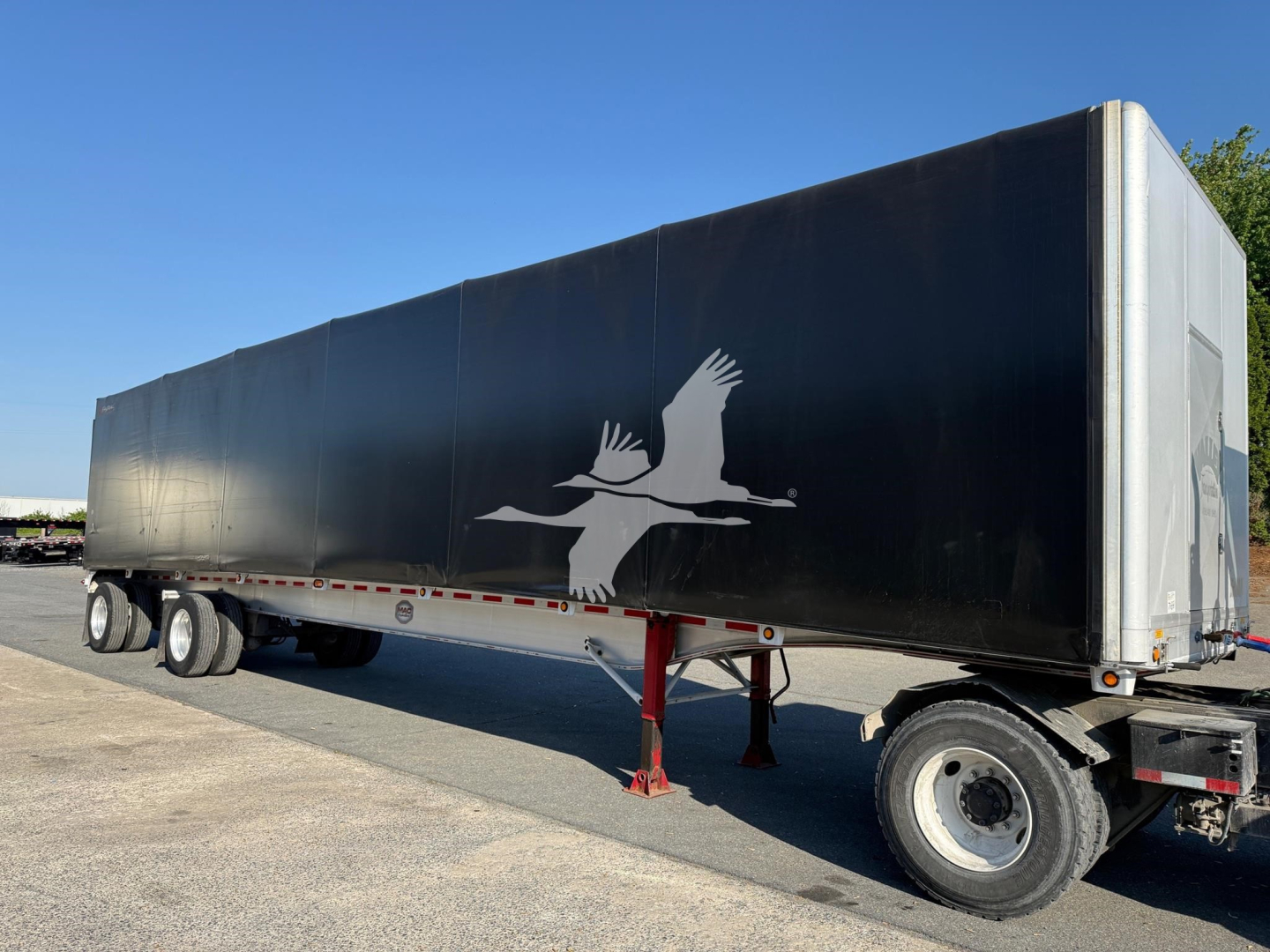 Trailer side view showing a black curtainside trailer with a white silhouette of a flying bird and red landing gear.