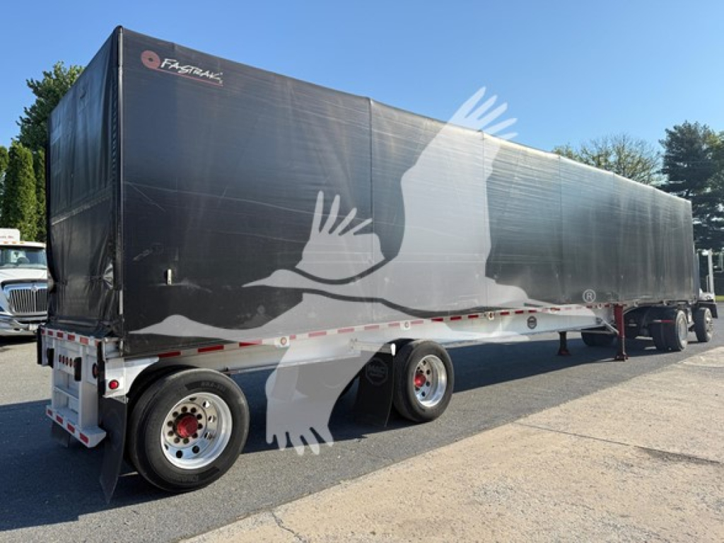 Mac aluminum flatbed trailer with curtain side in black, logo near front, large bird decal along side, rear dual-axle wheels, side rail and undercarriage visible.