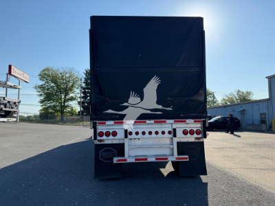 Trailer rear view showing large black curtain side with white bird graphic and rear lighting, mudflaps, and bumper; license plate area not visible.