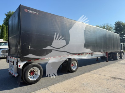 Mac aluminum flatbed trailer with curtain side in black, logo near front, large bird decal along side, rear dual-axle wheels, side rail and undercarriage visible.