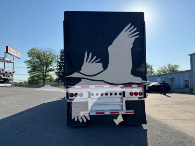 Trailer rear showing graphic of white birds on black curtain-side body, with rear underride guard and lights.
