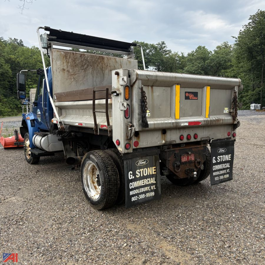 Dump truck rear view showing dump bed and plow-ready International DuraStar 4300 with Wing. License plate area and tailgate with yellow caution markings, dual rear wheels, truck bed dirt/grime.