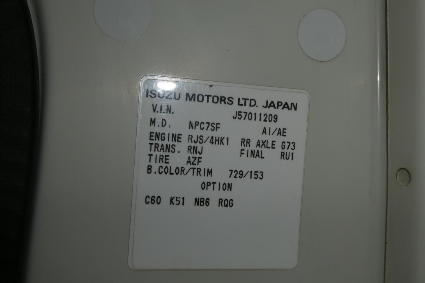 Vehicle label on Isuzu/GM truck showing VIN J8DC4B16657011209, M.D. NPC75F, ENGINE RJS/4HK, TRANS RNJ, FINAL RU1, TIRE AZF, B.COLOR/TRIM 729/153, OPTION C60 K51 NB6 RQG.
