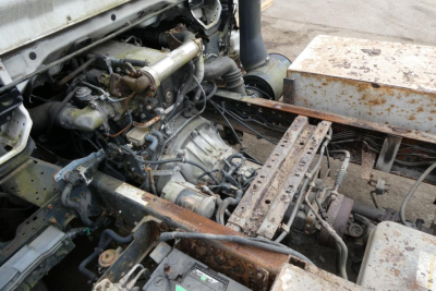 Truck engine bay showing exposed drivetrain components and rusted frame beneath cab of a 2005 GMC W4500. Visible items include engine block, hoses, and metallic chassis with brown rust patches.