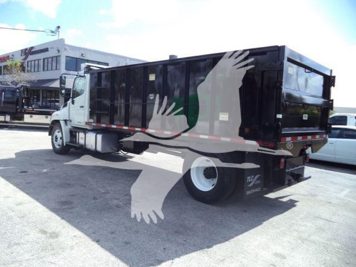 Dump truck body on a 2016 Hino 268A with black dump bed and white cab, side view showing stock trailer, no visible text on the side.