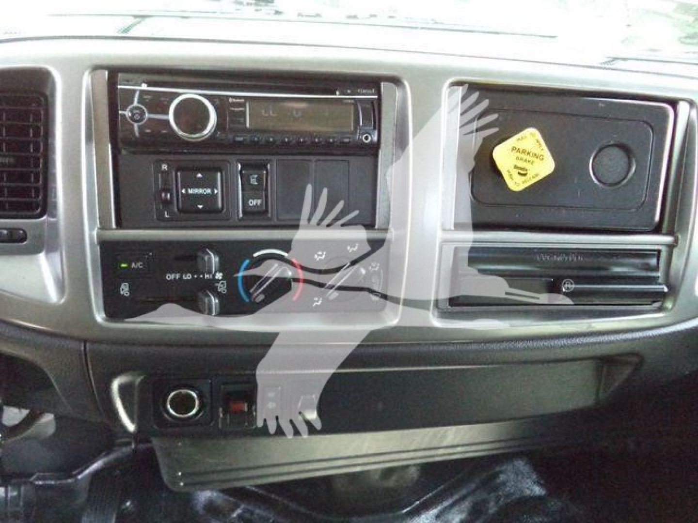 Dashboard of a 2016 Hino 268A cab showing radio/CD unit, climate controls, dashboard switches, and a yellow maintenance sticker on a panel.