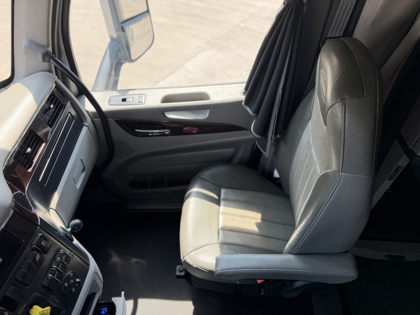 Peterbilt 579 cabin interior image showing driver seat and dashboard with light gray upholstery and window controls.
