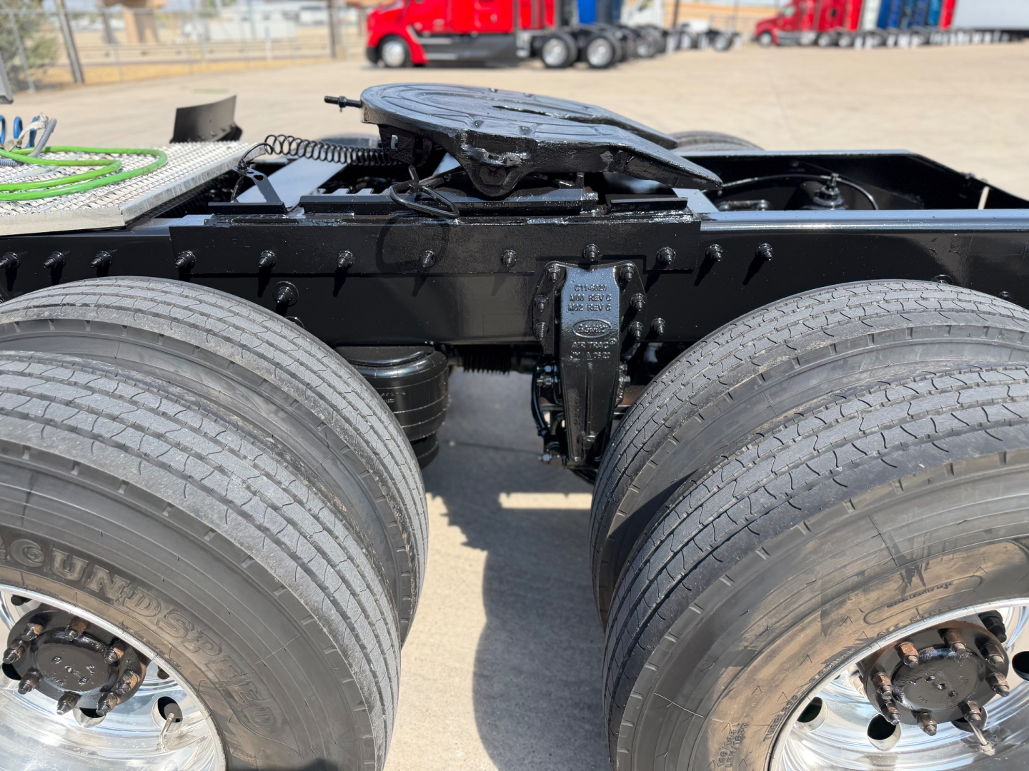 Peterbilt 579 truck chassis with rear dual wheels and fifth wheel visible in center; black frame and components; dual rear axles; tires show treads; part of towing yard in background.
