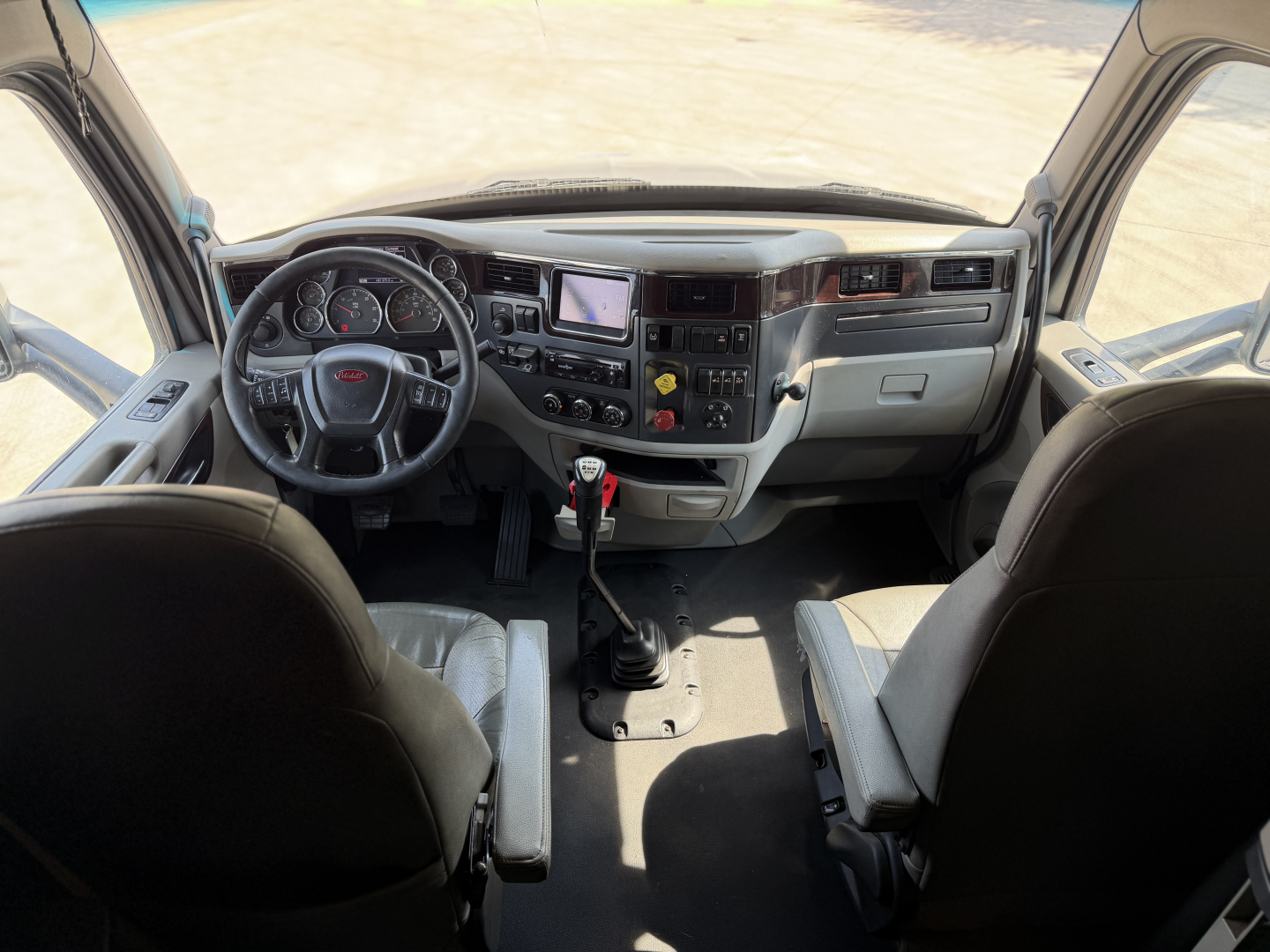Peterbilt 579 driver's cockpit interior showing steering wheel, dashboard, center console, touchscreen display, gear shifter, and seating.