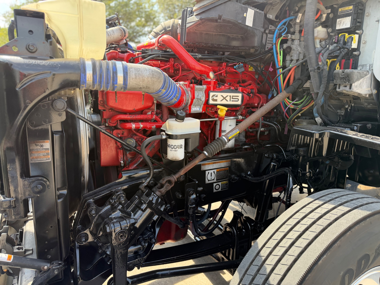Peterbilt 579 engine bay showing red 6-cylinder engine with blue silicone hose, white coolant reservoir, and various wiring harnesses.