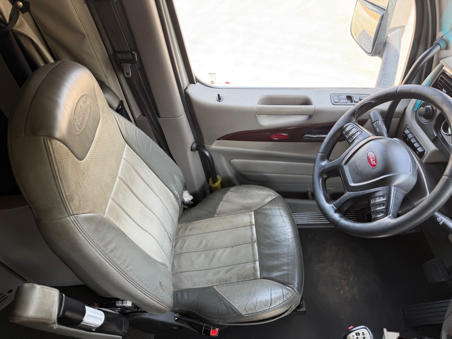 Peterbilt 579 truck interior showing steering wheel, driver seat, and dashboard with light gray seats and beige door trim.