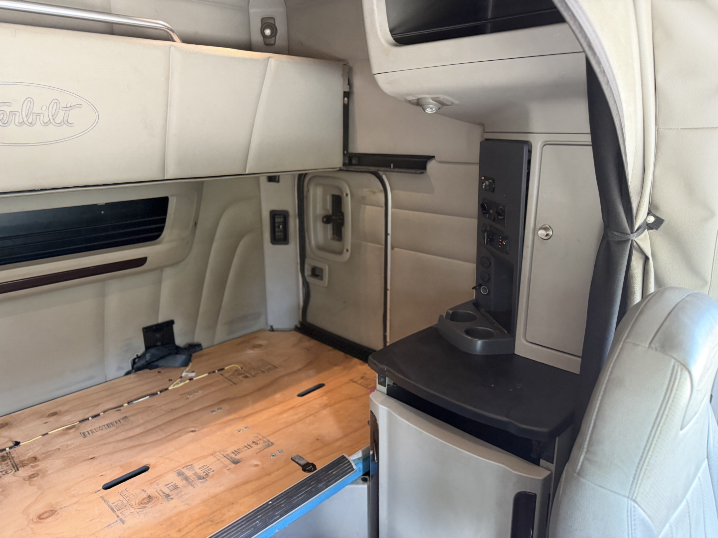 Peterbilt 579 sleeper cab interior showing storage cabinets, wood floor panel, and control console with cup holder.