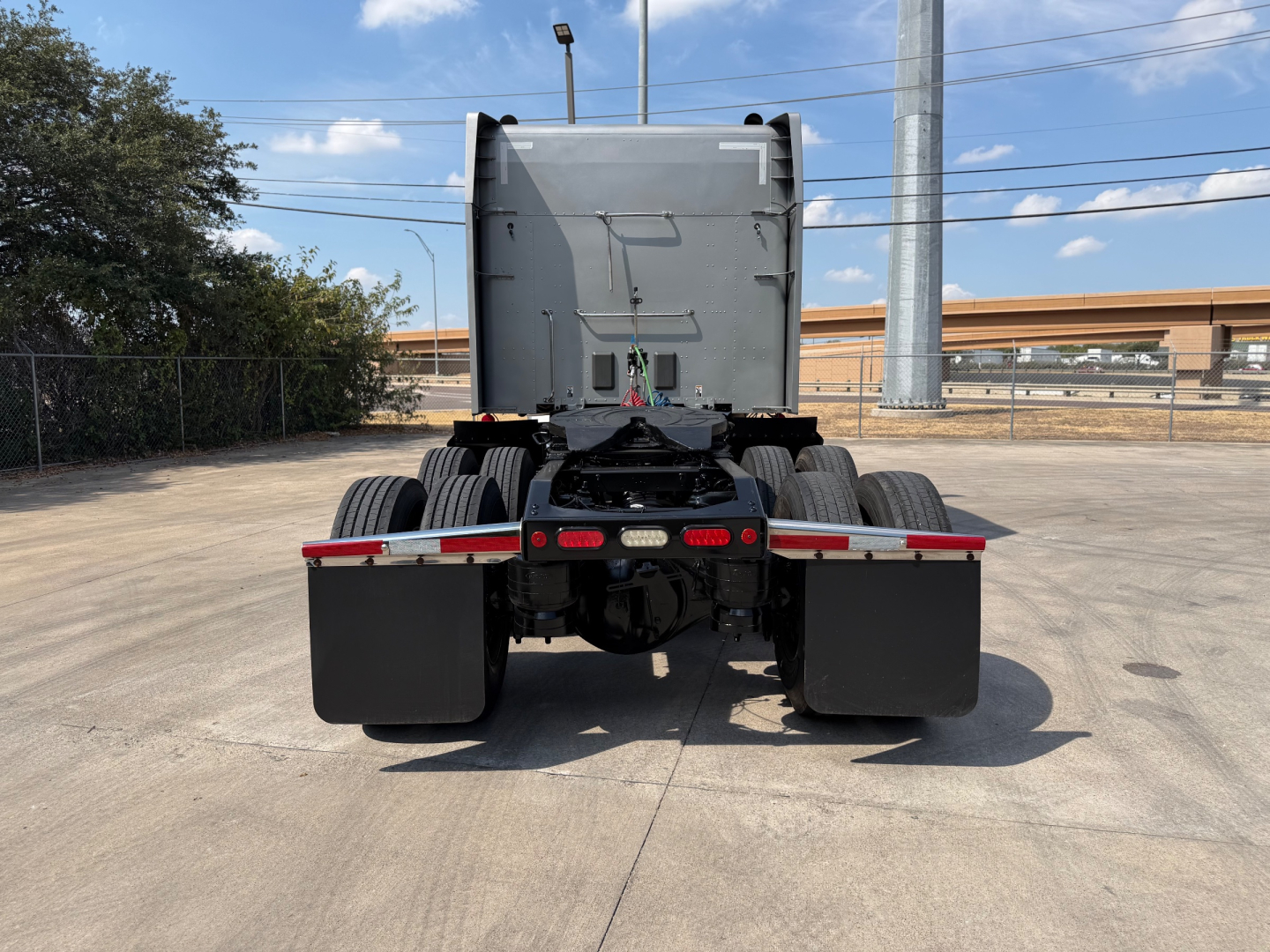 Peterbilt 579 tractor rear view showing fifth wheel and dual rear axles, gray cab, black fenders, and red rear lights.