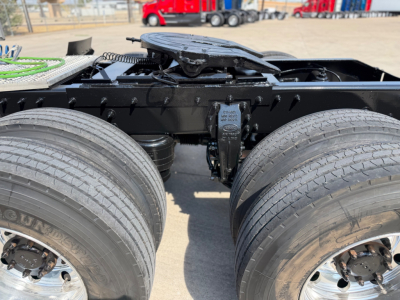 Peterbilt 579 truck chassis with rear dual wheels and fifth wheel visible in center; black frame and components; dual rear axles; tires show treads; part of towing yard in background.