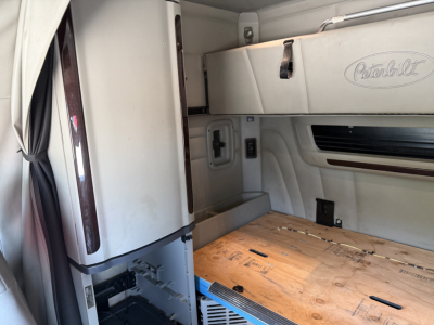 Peterbilt 579 sleeper cab interior showing cab wall with Peterbilt logo, side storage, and plywood floor panel in cargo area.