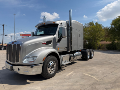 Peterbilt 579 tractor unit in a light gray color, front left angle showing cab, exhaust stacks, and fuel tanks; no visible branding text on image other than general shapes.