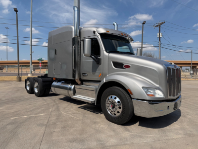 Peterbilt 579 tractor in a parking lot, silver exterior, sleeper cab, chrome exhaust stacks, large front chrome grille, dual rear axles.
