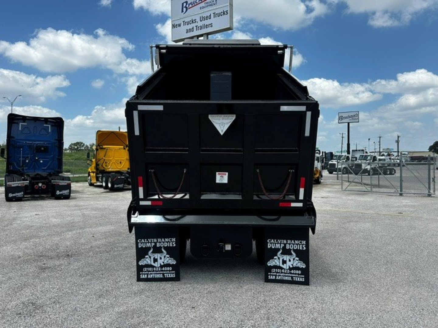 Truck dump bed hitch area of a 2027 Mack MD7 dump truck showing rear tailgate and mud flaps with logos and warning label.