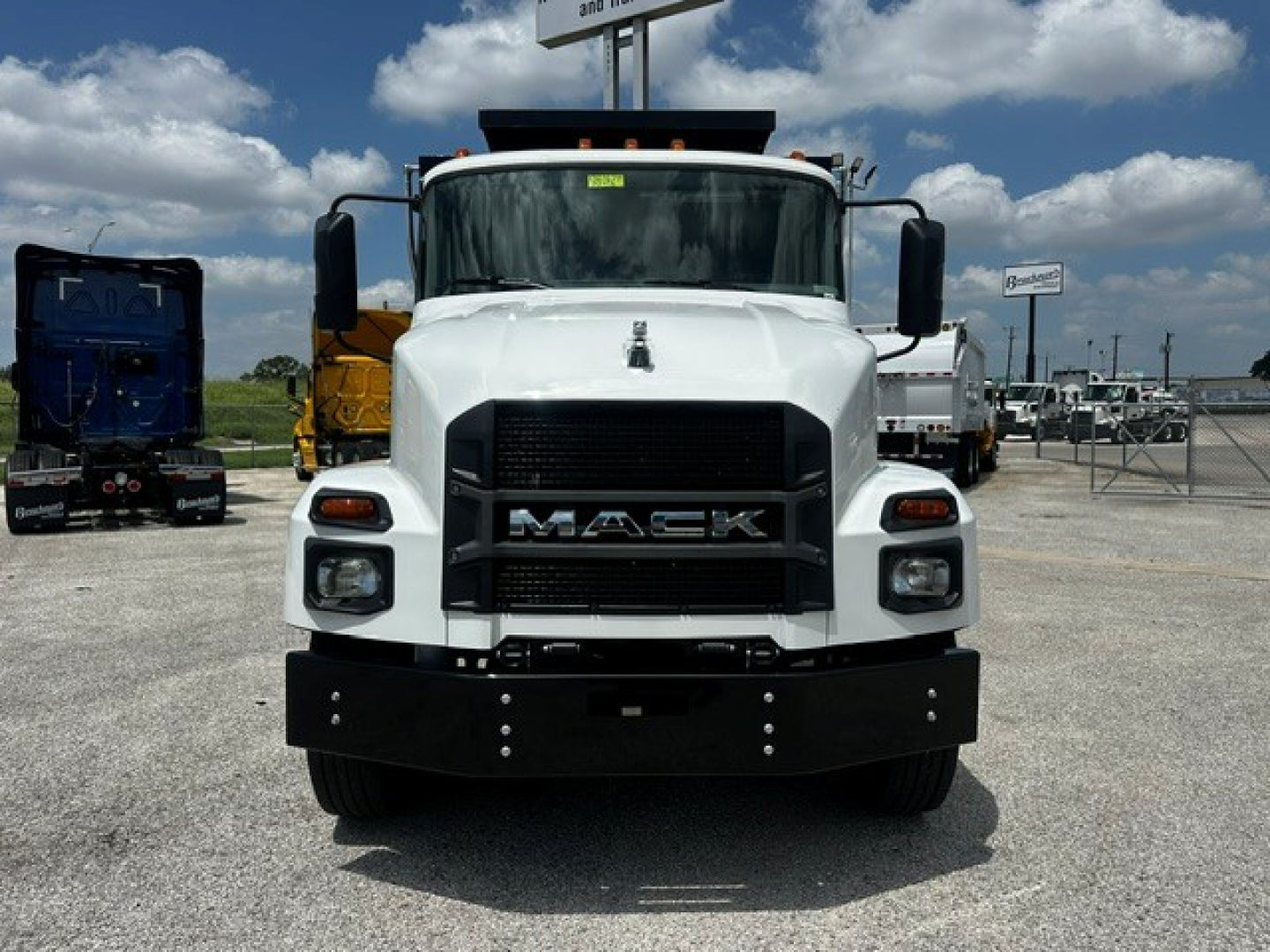 Front view of a white 2027 Mack MD7 dump truck showing large black grille with MACK emblem, bumper, headlights, and side mirrors.