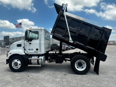 Truck side view of a 2027 Mack MD7 dump truck with dump bed raised, white cab, black dump bed, in a lot.