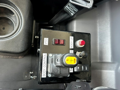 Dash-mounted control box with yellow knob and red button labeled BODY CONTROL, PTO, BOOT UP, and TA; part of Mack MD7 truck interior view