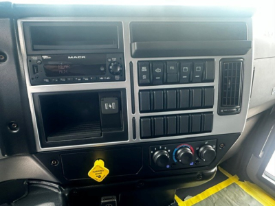 Dashboard interior of a Mack MD7 truck showing radio unit, climate controls, and multiple switches; yellow PTO/air accessory pull handle visible.