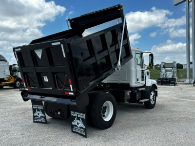 Mack MD7 dump truck with hydraulic tilting dump bed raised, white cab, black dump body, rear view showing taillights and mud flaps.
