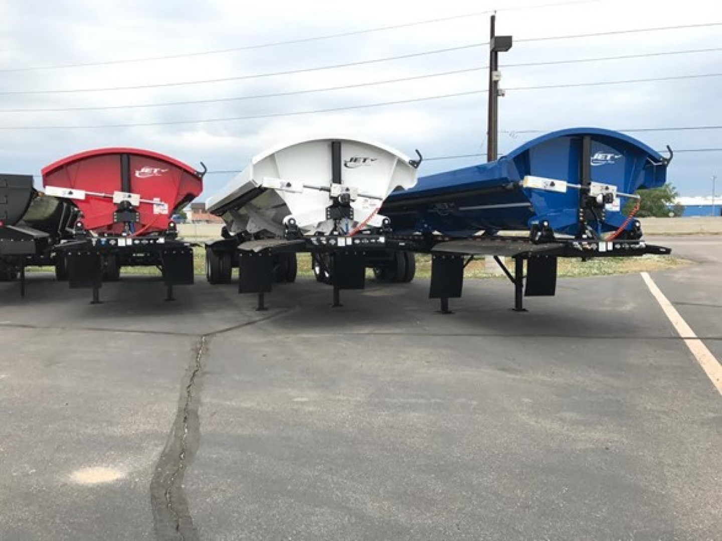 Jet side dump trailers with flex corners and four pivot points per side, in red white and blue, parked in a lot.