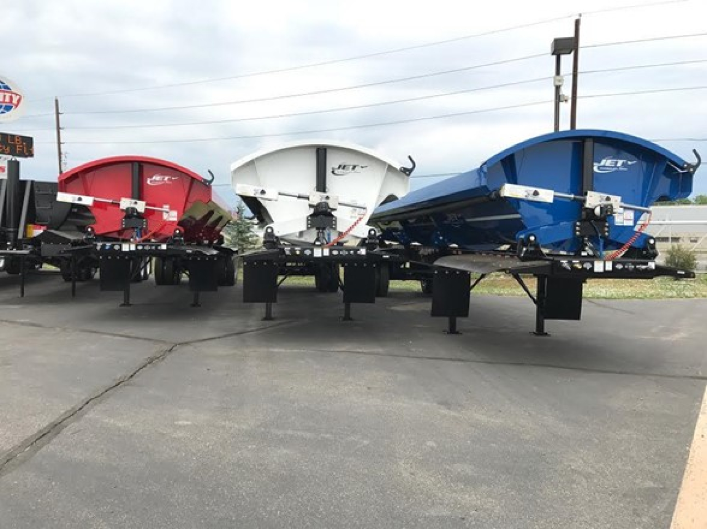 Jet SIDE DUMP trailers in red, white, and blue with 4 pivot points per side, viewed from the rear on a dealership lot.