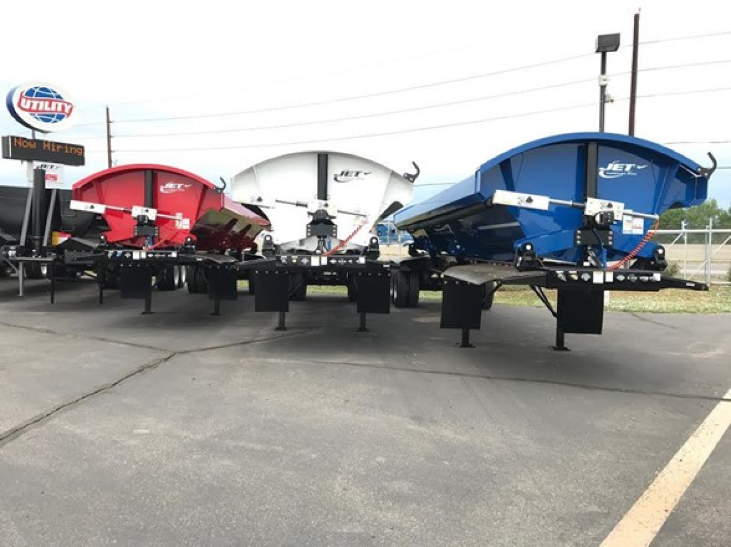 Jet side dump trailers in red, white, and blue colors lined up in a dealership lot showing 4 pivot points per side.