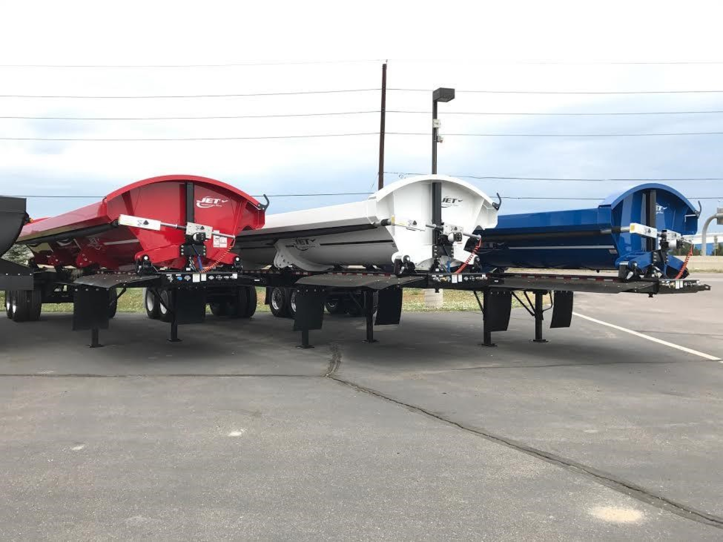 Jet Side Dump trailers in red, white, and blue parked on a lot; side dump mechanisms visible with undercarriage and wheels.