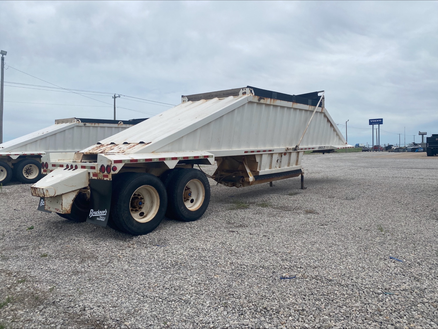 Dump trailer with skeletal frame and twin axles showing Armor Lite SBD40 type, long flatbed with side rails, gravel lot in background.
