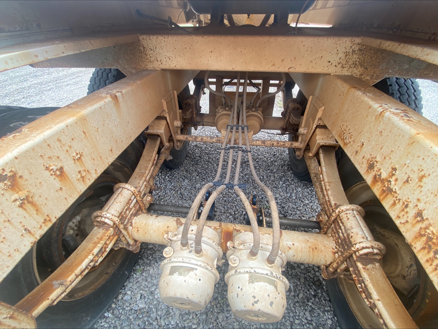 Truck chassis view showing the axle suspension with rusted frame rails and multiple air/brake lines connected to a central component.