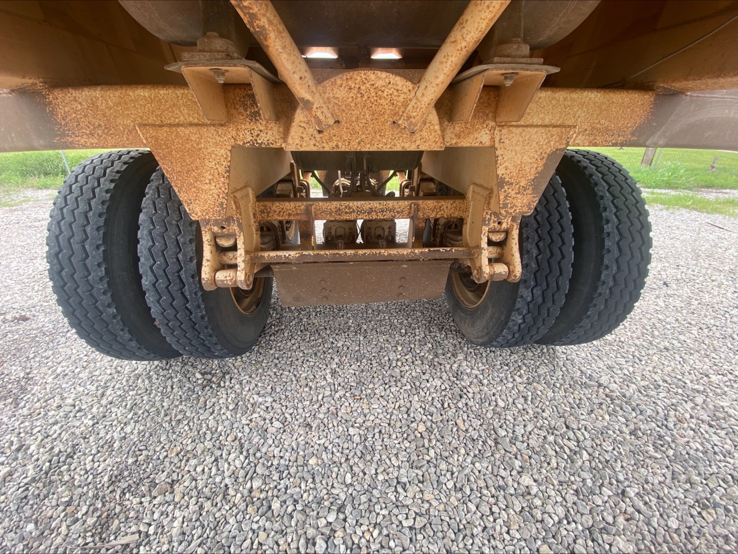 Trailer axle assembly and suspension undercarriage with dual tires and rust-colored components; view from rear undercarriage.