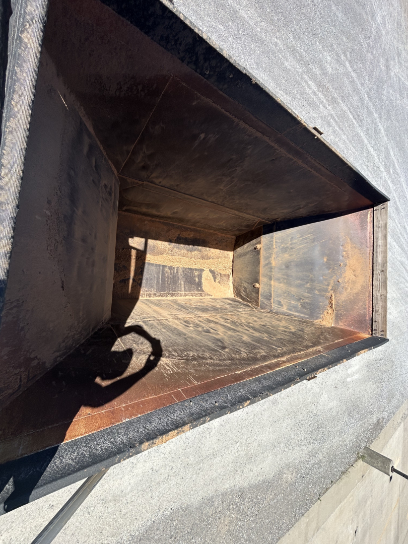 Trailer dumping bed interior showing rusty metal walls and empty chute near open top.