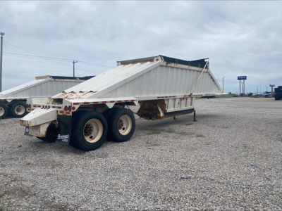 Dump trailer with skeletal frame and twin axles showing Armor Lite SBD40 type, long flatbed with side rails, gravel lot in background.